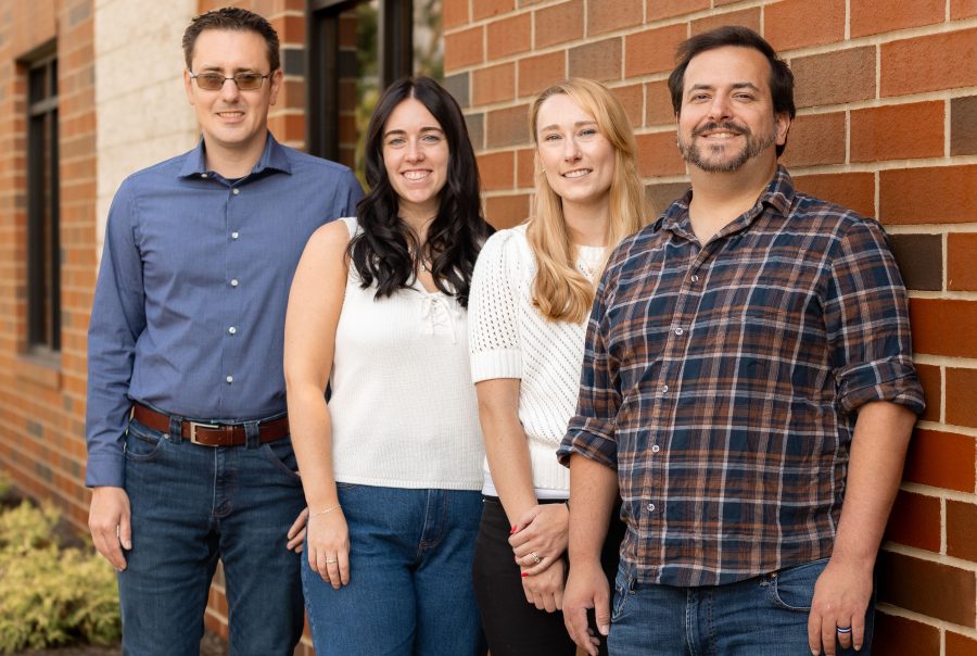 The staff of Ladderside Marketing outside along a credit union's brick wall - left to right is Josh Ondo, Maggie Hughes, Hallie Shaw Clark, and Ryan Lucas